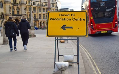 arrow pointing to covid vaccination centre with red London bus in background